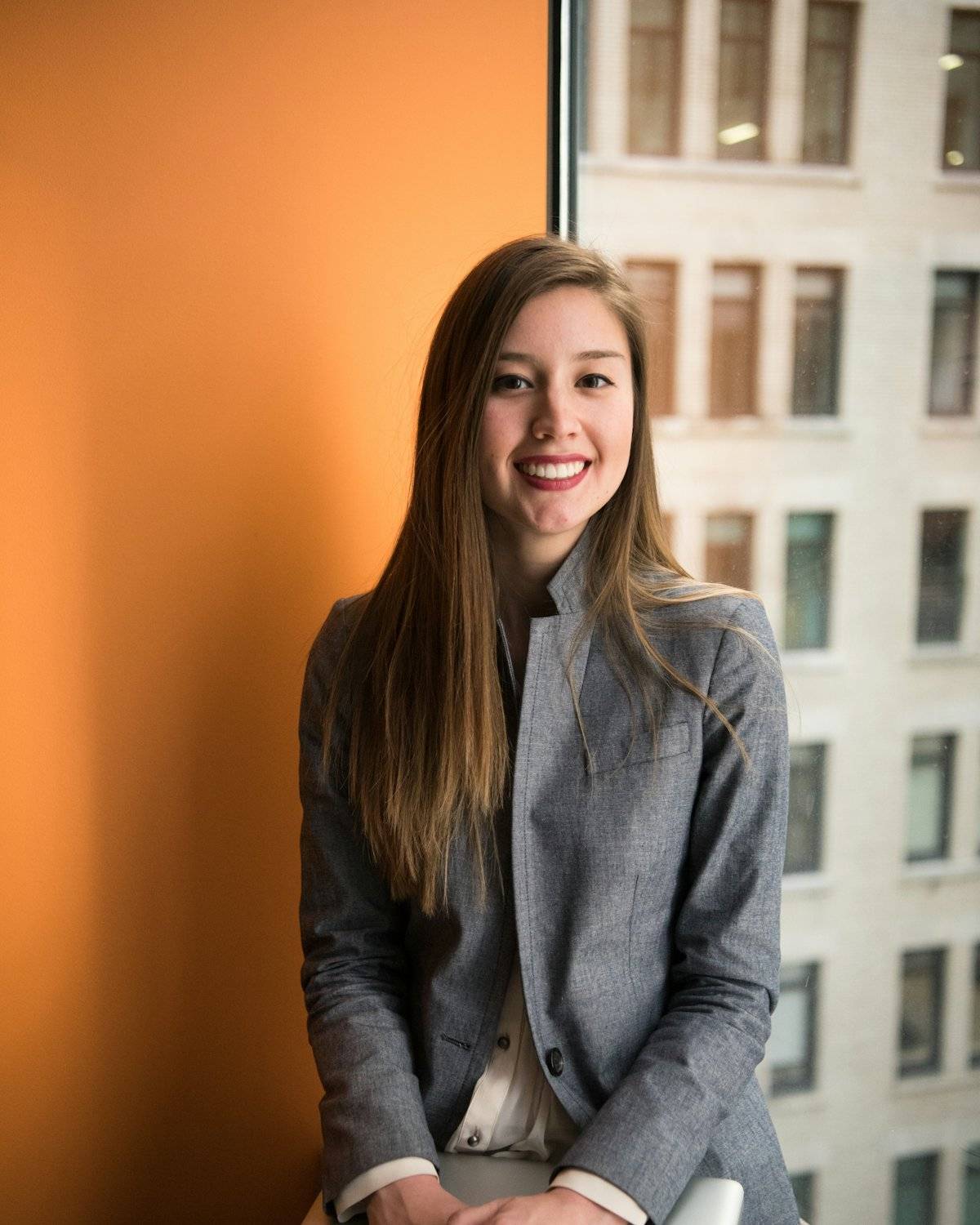 Smiling professional in a grey blazer sitting by an office window